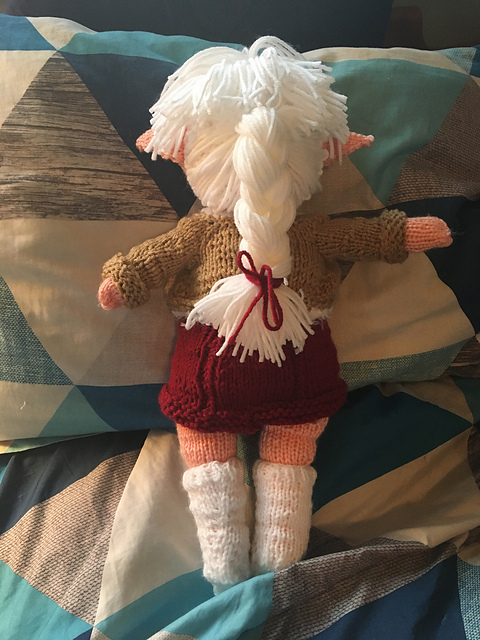 A knit doll of of Alisaie from Final Fantasy XIV, seen from the back. This view shows off the length of her cropped jacket and dress, as well as her braided white hair. Alisaie from FFXIV, back