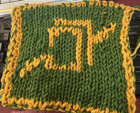 A knitted blanket square, featuring the the Astrologian job stone from Final Fantasy XIV. It looks like a stack of playing cards, outlined in gold, on a green background. This is the front view. FFXIV Astrologian Square, front