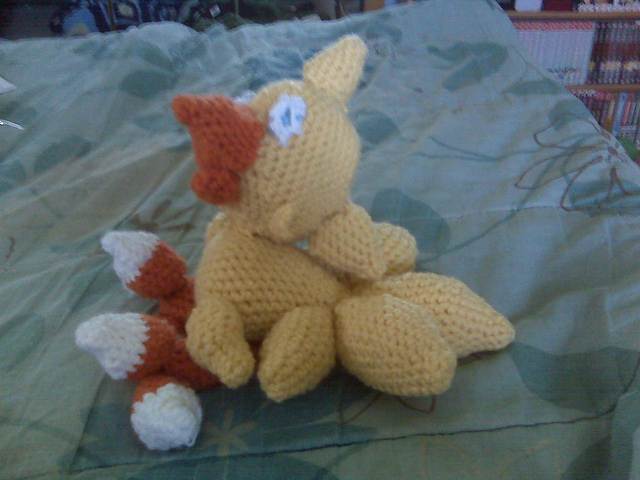 A crocheted baby chocobo. Chocobos look a bit like chickens. This one is yellow in color with orange legs and blue eyes. Baby Chocobo