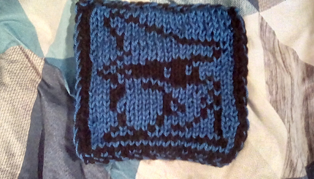 A knitted blanket square, featuring the iconic Black Mage sprite from the Final Fantasy video game series. The mage is dressed in a robe and tall pointy hat, with only glowing eyes showing of his face. The sprite is knit in black, on a blue background. Black Mage Square