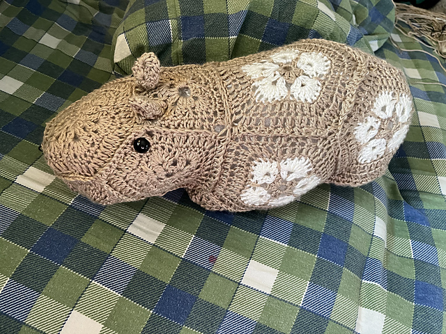 A crocheted softie of a Capybara. The toy is made up of African Flower motifs in tan (main color) and cream (contrast color). Capybara