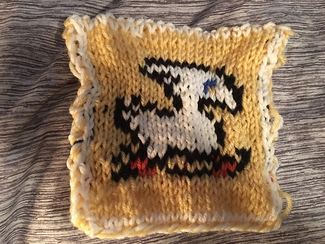 A knitted blanket square, featuring the iconic Chocobo sprite from the Final Fantasy video game series. The white chocobo is outlined in black against a yellow background. This is the back view. Chocobo Square, back