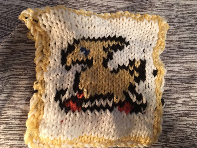 A knitted blanket square, featuring the iconic Chocobo sprite from the Final Fantasy video game series. The yellow chocobo is outlined in black against a white background. This is the front view. Chocobo Square, front