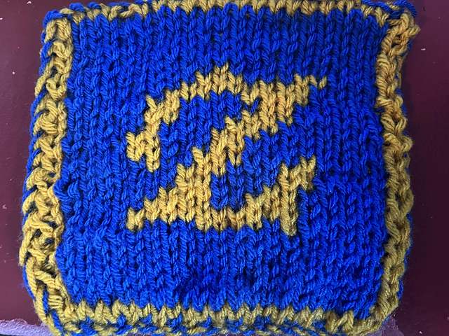 A knitted blanket square, featuring the the Gunbreaker job stone from Final Fantasy XIV. It looks like a gold stylized 'Z' on a royal blue background. This is the front view. FFXIV Gunbreaker Square, front