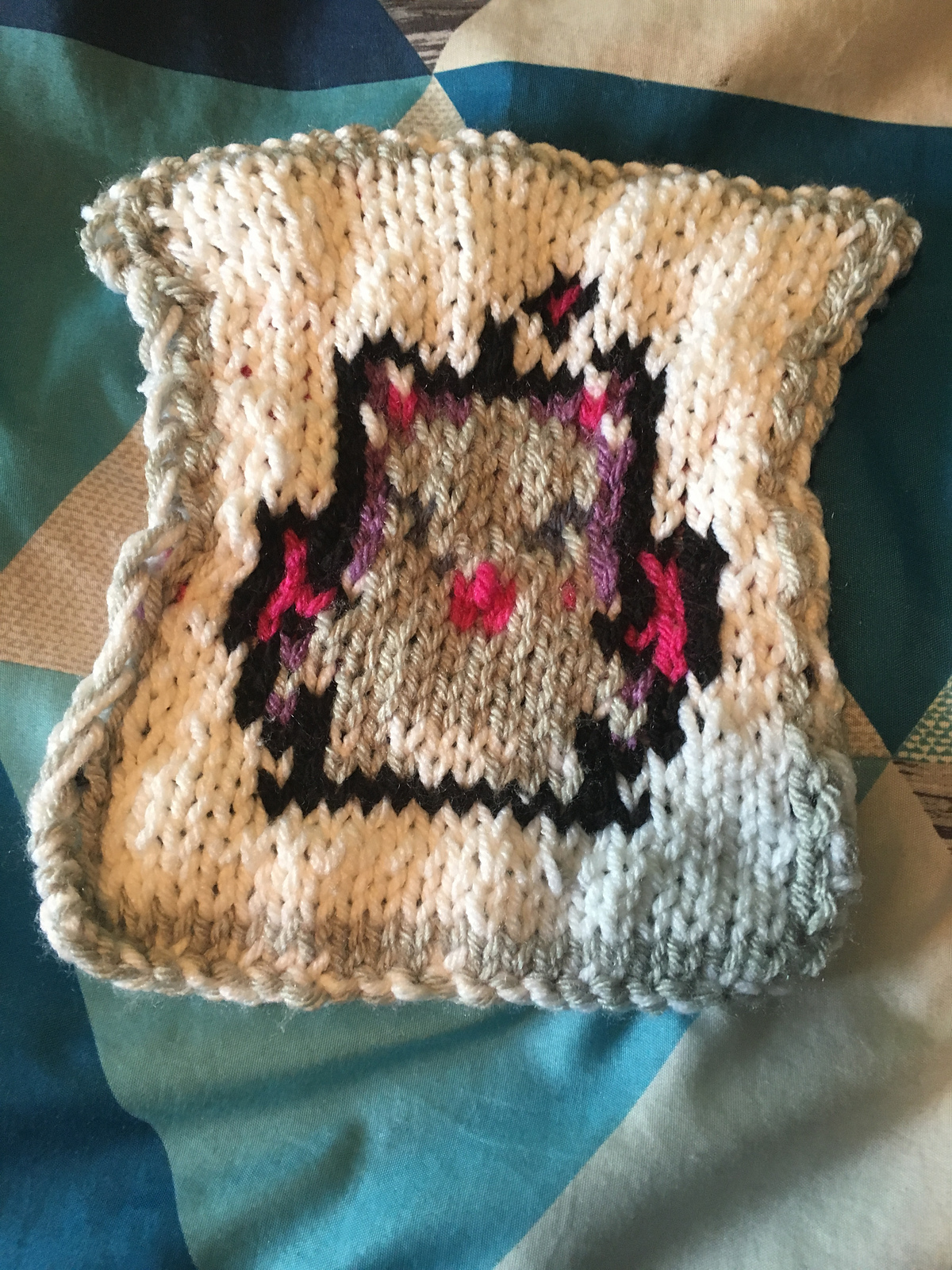 A knitted blanket square, featuring the iconic Moogle sprite from the Final Fantasy video game series. The gray moogle is outlined in black against a white background, and has pink wings and purple shadowing on its face. This is the back view. Moogle Square, back