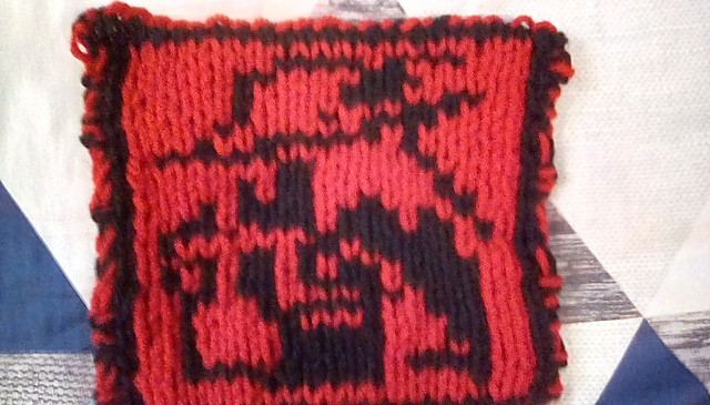 A knitted blanket square of the Red Mage sprite from the first Final Fantasy game. This is the front view, showing the character outlined in black on a red background. Red Mage Square, front