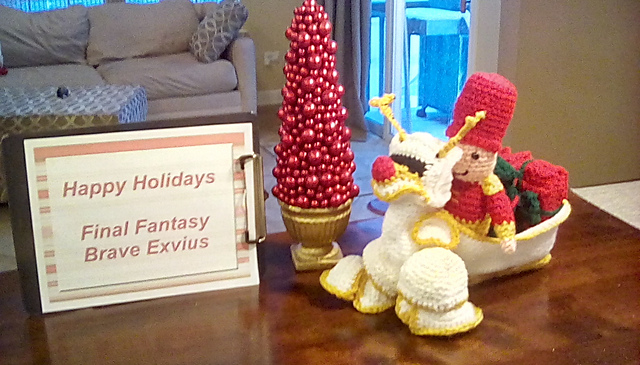 A crocheted softie of the White Knight Noel unit from Final Fantasy Brave Exvius. It's a nutcracker in a sled pulled by a mechanical white reindeer. Two large presents are in the sled behind Noel. White Knight Noel from FFBE