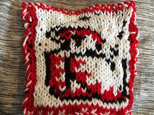 A knitted blanket square, featuring the iconic White Mage sprite from the Final Fantasy video game series. The White Mage is outlined in black, wearing a white hooded robe with red at the hems, and is on a white background. Red hair peeks out from under the hood. This is the front view. White Mage Square