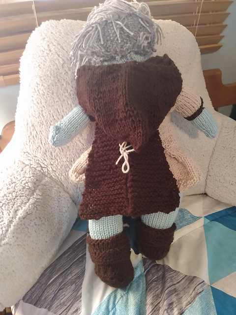 A knitted doll of one of my FFXIV characters, Windy Storm, seen from the back. She's got light green skin and silvery-gray short hair. This view shows off the hooded cape very well: it's split down the middle with light brown lacing. I still need to place more strands of hair on Windy's head, oops. Windy Storm, a Warrior of Light from FFXIV, back